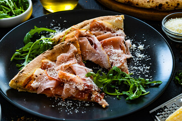 Wall Mural - Pizza with cured ham, parmesan cheese and arugula on black table