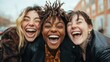 © JoxyAimages - Three diverse women share a moment of laughter and joy outdoors, showcasing their unique styles and emotions while embracing the spontaneity of friendship in a lively environment.