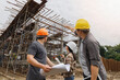 © skarie - Team of construction workers discussing project details with blueprint in construction site.