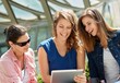 © nyul - Young female friends using tablet computer outdoors, smiling happy.