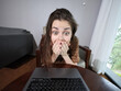 © SHOTPRIME STUDIO - Surprised woman reacting to unexpected news while working on her laptop in a cozy room, showcasing emotions of shock and excitement