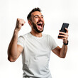 © miss irine - Happy young man celebrates online success with mobile phone. Excited male in casual clothing holds smartphone, shows winning gesture. Joyful expression on face. Studio shot against plain background.