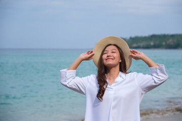 Wall Mural - Portrait image of a woman with white t-shirt holding hat while strolling by the sea