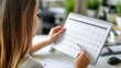 © nanskyblack - Young professional woman in business casual attire organizing her calendar for upcoming meetings in a stylish office.