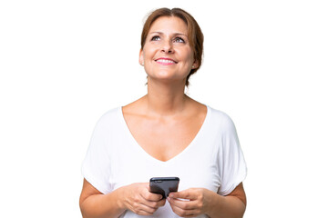 Wall Mural - Middle-aged caucasian woman over isolated background using mobile phone and looking up