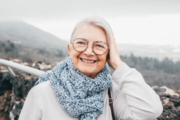 Wall Mural - Portrait of attractive smiling senior woman with eyeglasses  outdoors in a foggy winter day