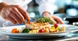 © BerkahStock - Chef plating grilled fish with vegetables on a white plate.