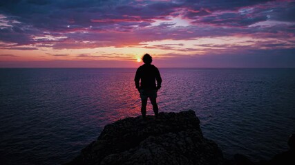 Fototapete - Sunset view from a rocky shore with a silhouette of a person enjoying nature's beauty