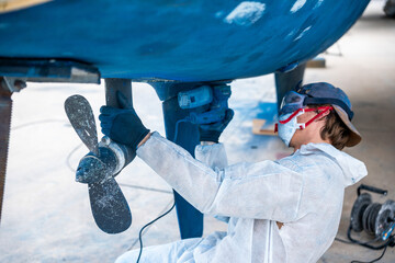 a man polishing the side of the hull of a blue ship.