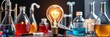 © Sathaporn - A modern science experiment setup with a light bulb at the center surrounded by various laboratory equipment and a miniature graduation cap, glowing light, science experiment