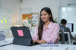 © amnaj - Asian businesswoman smiling while working with tablet at her desk in modern office
