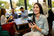 © Mediteraneo - Woman using her phone in the restaurant. Her friends are in the background.