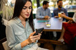 © Mediteraneo - Woman using her phone in the restaurant. Her friends are in the background.