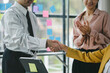 © amnaj - Business partners shaking hands after closing a deal while their colleague is clapping, celebrating the agreement