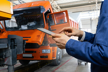 Poster - Serviceman with digital tablet on the background of the truck in the car service.