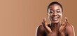 © Prostock-studio - African American woman with a joyful expression is pampering her skin as part of her beauty routine. She showcases her natural glow against a warm, neutral background