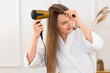 © Pixel-Shot - Beautiful woman drying her hair with round brush in bathroom