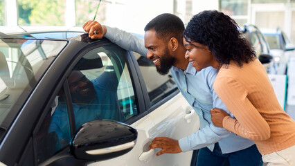 Wall Mural - New Car. Excited Black Spouses Looking At Their New Automobile In Dealership Office, Happy African American Couple Choosing Luxury Vehicle In Showroom, Checking Automobile Interior, Closeup