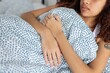 © Xavier Lorenzo - Young woman embracing pillow while lying in bed, experiencing abdominal pain or discomfort