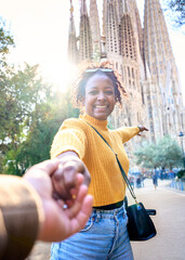 Wall Mural - Vertical. POV of young mixed race couple holding hands in front of Sagrada Familia in Barcelona. Smiling girlfriend looking camera on street of city enjoying vacation happy and smiling. Tourism people