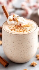 A creamy beverage is topped with fluffy whipped cream and a sprinkle of cinnamon, served in a rustic mug. The background features warm colors and cozy décor elements