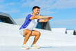 © muse studio - Fitness enthusiast performs squats outdoors with modern architecture in the background on a clear day