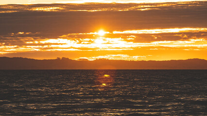 Wall Mural - Colourful vibrant red orange golden sunset into sea ocean water in New Zealand