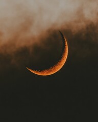 Wall Mural - orange crescent moon partially hidden behind dark clouds at night