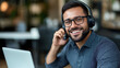 © Andres Mejia - Smiling male call center agent working on laptop with headset in office