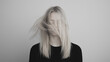 © pattozher - Lost in Thought: A woman with long blonde hair, partly covering her face, stands against a muted background in a moment of introspection, inviting contemplation and interpretation.