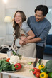 © crizzystudio - Loving couple having fun and sharing a joyful moment while preparing a healthy meal together in their modern kitchen, surrounded by fresh vegetables