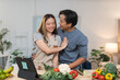 © crizzystudio - Young asian couple embracing each other while preparing fresh ingredients for a healthy meal in a modern kitchen, happily using a tablet to follow their favorite recipe