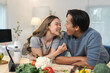 © crizzystudio - Young asian couple enjoying quality time while preparing a healthy meal in a modern kitchen, with the woman playfully feeding the man with a fork, sharing smiles and laughter