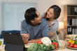 © crizzystudio - Young asian couple cooking together in a cozy kitchen, checking recipes on a tablet, smiling and enjoying the process of preparing a delicious, healthy vegetarian meal