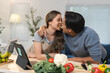 © crizzystudio - Young asian couple having fun sharing a cucumber slice while preparing a healthy meal together in their modern kitchen, using a digital tablet for recipe