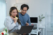 © crizzystudio - Happy asian couple holding credit card and using laptop computer making online shopping or payment banking at home together, technology money wallet and online payment concept