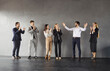© Studio Romantic - Group of company employees congratulating happy male colleague on job well done applauding standing in a row on gray wall background. Business people group clapping to young smiling man in office.