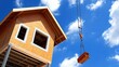 © DSimage - A towering crane hoists a quaint house into the air, defying gravity as it prepares for a new home, surrounded by blue skies and curious onlookers.