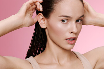 Young woman with wet hair and natural makeup poses against a pink background, expressing confidence and beauty in a contemporary style