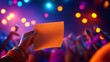 © movinglines.studio - Hand holding orange card with bokeh lights and festive crowd in colorful background.