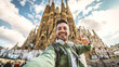 © Davide Angelini - Happy tourist visiting La Sagrada Familia, Barcelona Spain - Smiling man taking a selfie outside on city street - Tourism and vacations concept