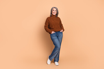 Wall Mural - Elegant senior woman in casual jeans and sweater posing confidently against a beige background