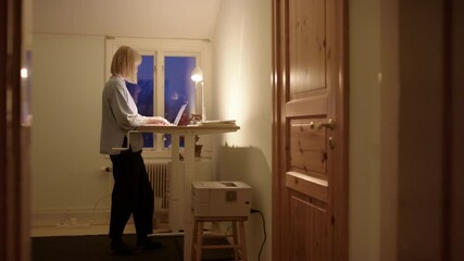 Woman hustling online on laptop at night use standing desk for improved posture