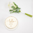 © Niko_Dali - A celebratory scene featuring a simple white cake decorated with the words Hello 35 in gold. A small bouquet of white calla lilies and eucalyptus rests beside it.