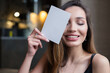 © RooM The Agency - Smiling woman with her eyes closed holding a blank card in front of her face
