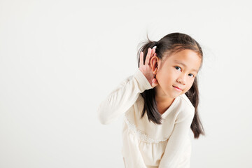 Wall Mural - Portrait Asian young child smiling overhearing listening sound to gossip with attention with hand on ear studio shot isolated on white background with copy space hearing gesture, kindergarten kid girl