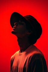 Wall Mural - A person wearing an oversized hat poses against a vibrant red background, with a side profile highlighting their features