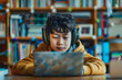 © Alberto Gonzalez  - Child in a yellow hoodie deeply focused on content on a laptop with headphones on in a library.