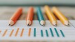 © Sirichai - Color Coded Pencils on Graph: Four sharpened pencils in orange and teal, arranged neatly on a lined paper showing a simple bar graph, representing concepts of planning, analysis.