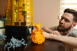© phoenix021 - Handsome bearded man admires how his 3d printer is working, finished figurines next to it